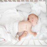White iTODOS flexible baby monitor mount with an 8-inch arm, clamped to a crib, holding a Nanit Pro baby monitor.