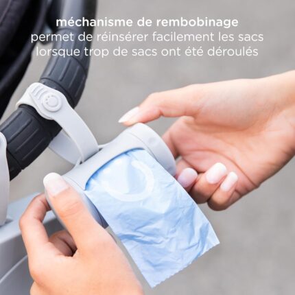 Gray retractable diaper bag dispenser with a roll of lavender-scented bags, clipped to a stroller handle.